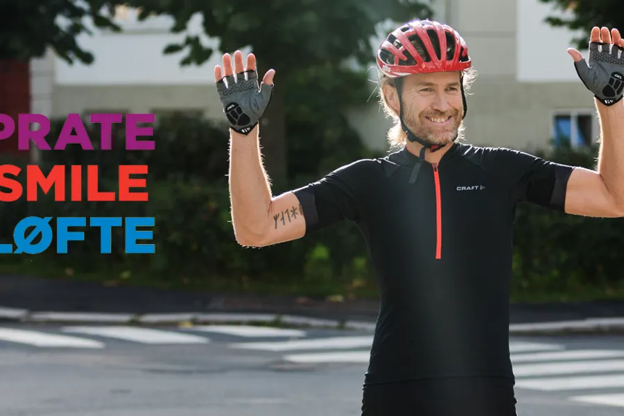 Syklist med hjelm som løfter armene og smiler. 